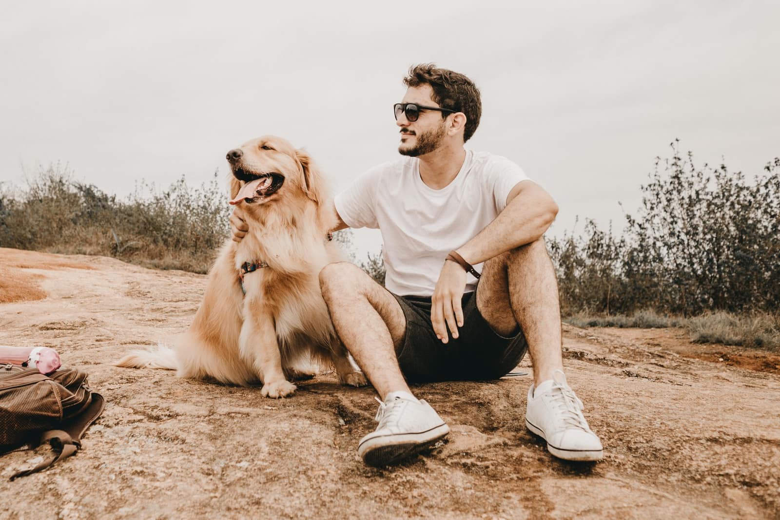 A man relaxes outdoors beside his golden retriever, the vet visits, grooming and supplies handled so they can enjoy the day.