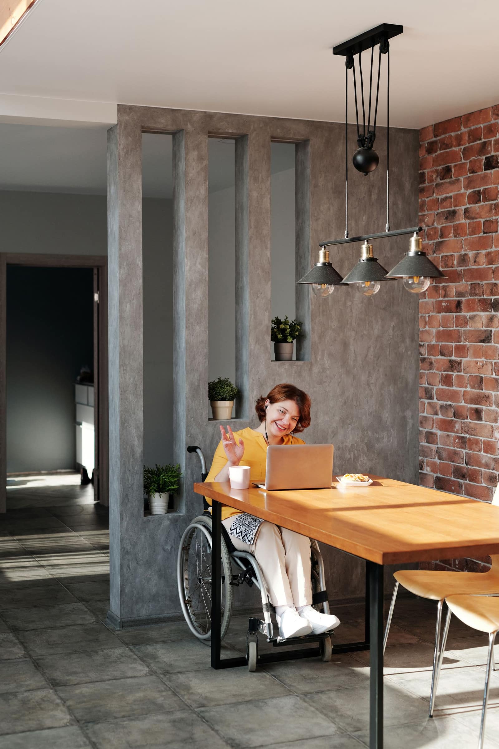 A smiling wheelchair-using member works from home with a coffee, the day's admin delegated and handled in the background.