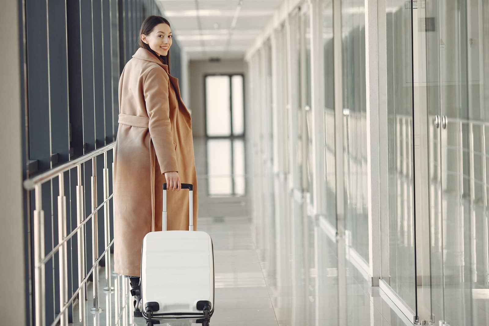 A traveler pauses with her suitcase in a bright airport concourse, her itinerary researched, booked and confirmed in advance.